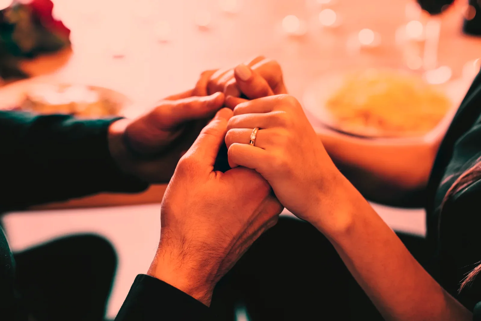A couple's hands intertwined across a dinner table, an engagement ring catching the light